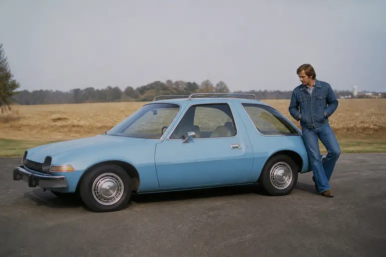 Une AMC Pacer bleue de 1970s garée au soleil, un homme inspectant le véhicule.