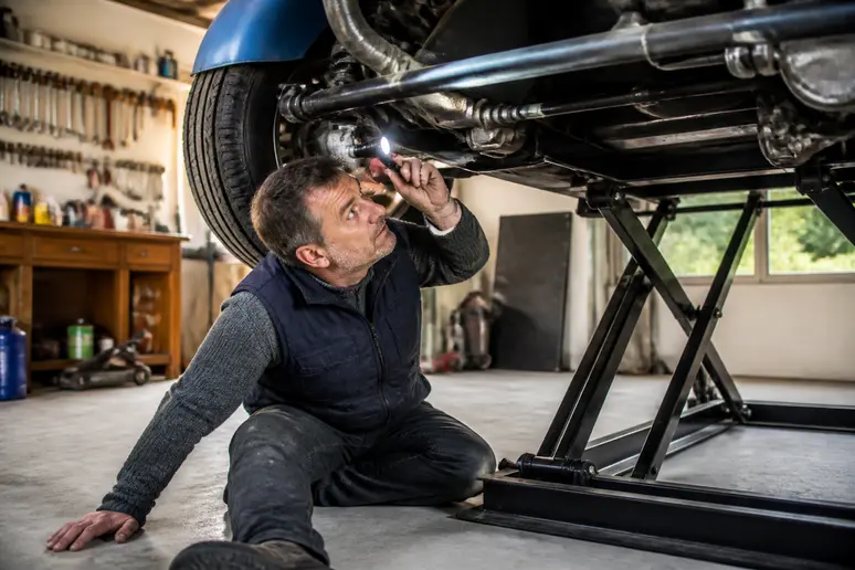 Un homme vérifie l'état du châssis d'un buggy de collection dans un garage, étape cruciale avant l'achat.