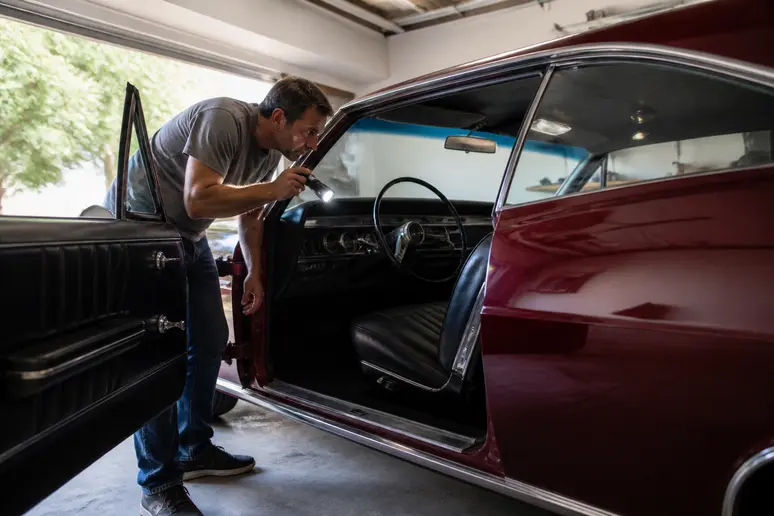 Un homme d'âge moyen examine l'intérieur d'une Chevrolet Impala 1967 dans un garage, vérifiant les détails du tableau de bord.