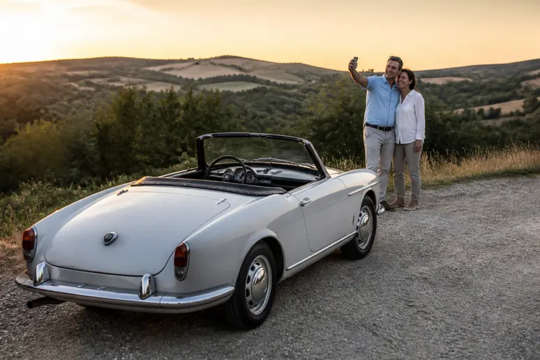 Un couple italien admirant une voiture sportive italienne vintage des années 50 dans la campagne toscane au coucher du soleil.