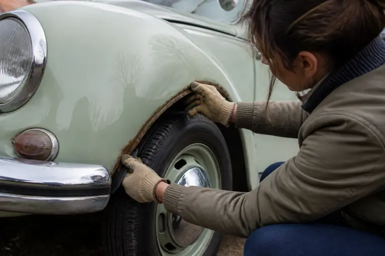 Mains gantées d'une femme examinant attentivement le passage de roue d'une Coccinelle ancienne à la recherche de rouille.