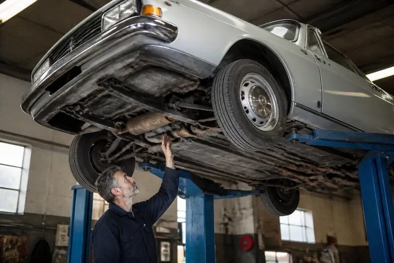 Inspection minutieuse des soubassements et du châssis d'une 504 cabriolet occasion sur un pont élévateur d'atelier