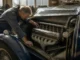 Un mécanicien inspecte le moteur d une bugatti ancienne dans un atelier baigné de lumière naturelle.