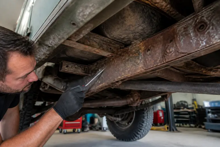 Inspection minutieuse du châssis et des longerons corrodés d'un range rover classic d'occasion.