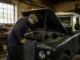 Un mécanicien inspecte le compartiment moteur d'un range rover classic occasion dans un garage lumineux.