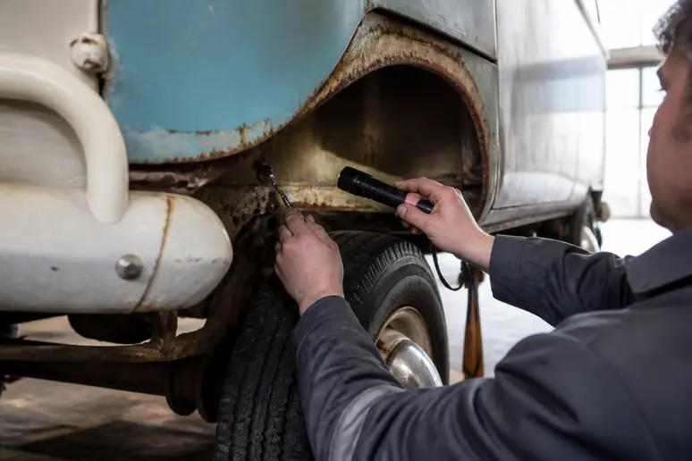 Inspection minutieuse de la corrosion structurelle sur le châssis d'un van volkswagen combi ancien avec une lampe torche