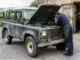 Un defender vintage garé près d'un atelier rural pendant une inspection mécanique en plein air.