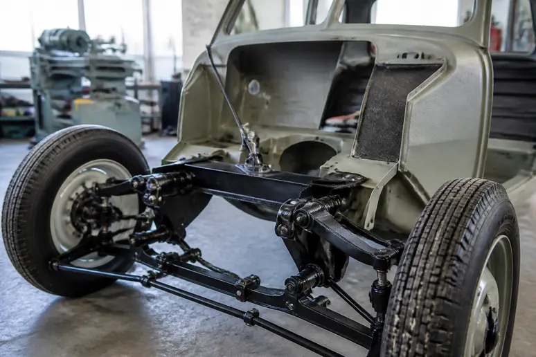 Châssis monocoque et suspension avant indépendante d'une Renault Juvaquatre ancienne en cours de restauration dans un atelier.
