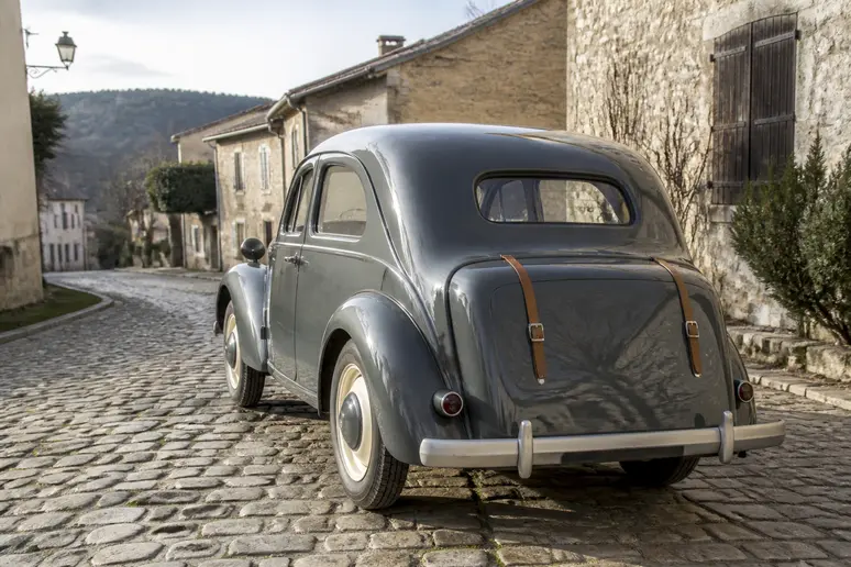 Vue arrière de trois quarts d'un coach Renault Juvaquatre montrant l'accès au coffre extérieur et la carrosserie d'époque.