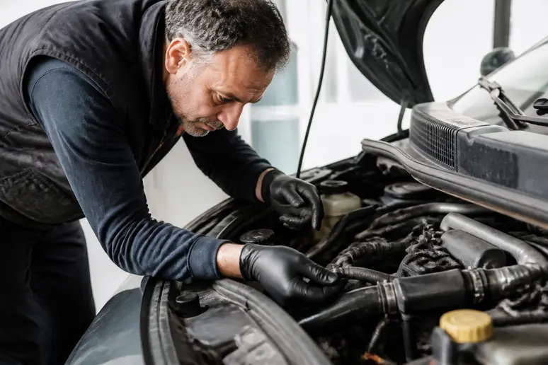 Un mécanicien examine le compartiment moteur d'un Renault Scénic II d'occasion dans un garage.