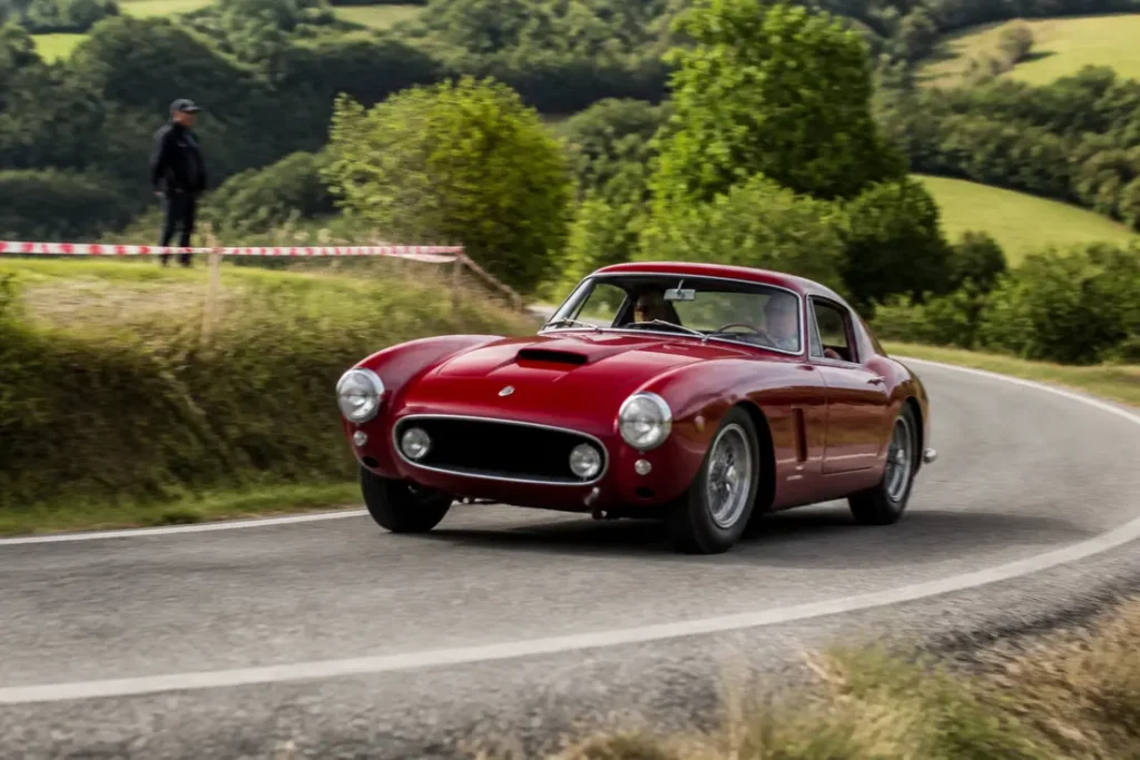 Une voiture de collection participe au tour auto 2026 parcours sur une route sinueuse.