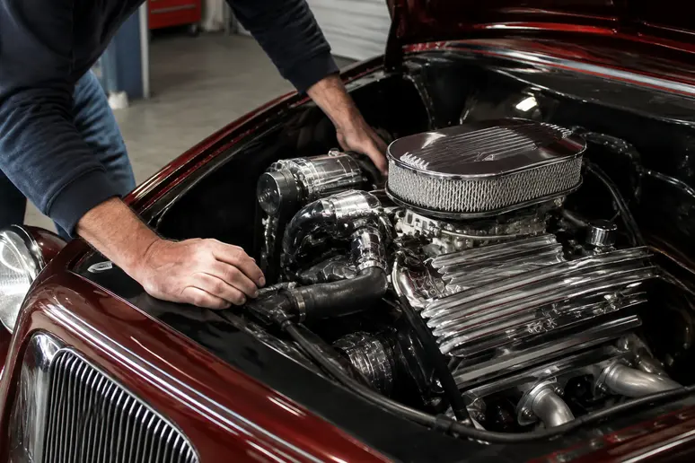 Mains d'un mécanicien inspectant le compartiment moteur d'un hot rod d'occasion dans un garage