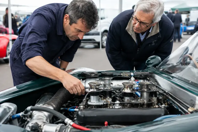 Un commissaire technique examine le moteur d'une voiture de course ancienne dans le paddock.